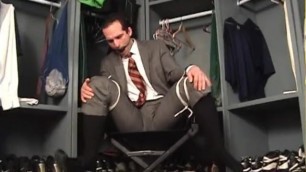 Suited man tied to chair ball gagged and struggling.