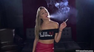 The girl wears a leather mini-skirt and a crop top and smokes a cigarette.